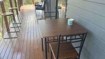 A wooden deck with a table and chairs, a railing, and a view of the outdoors.