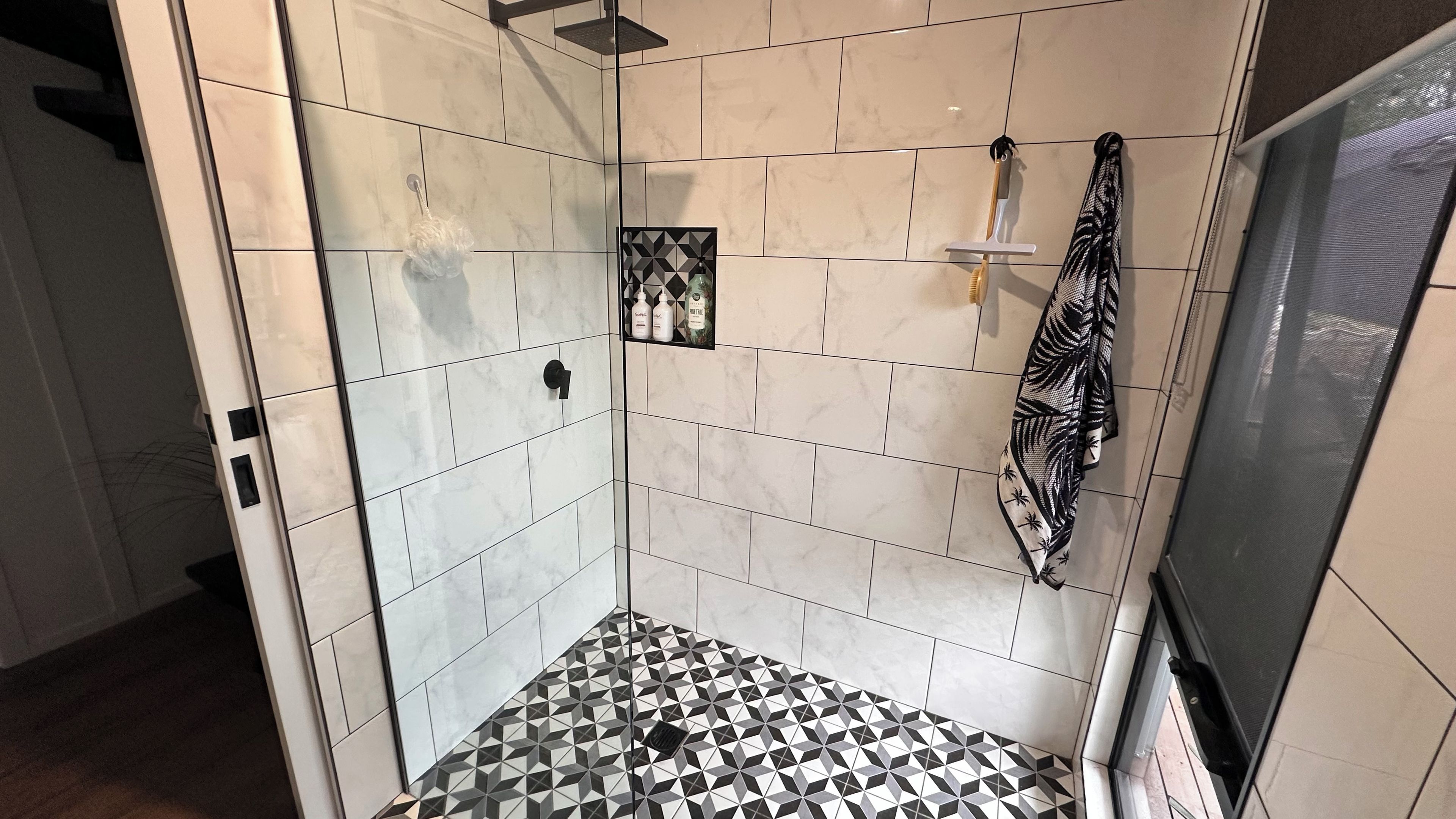 A bathroom with a tiled floor, a shower area, and a towel rack.