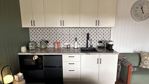 Eine kompakte Küche mit weißen Schränken, einem schwarzen Geschirrspüler, einer Kaffeemaschine und einer Uhr an der Wand.