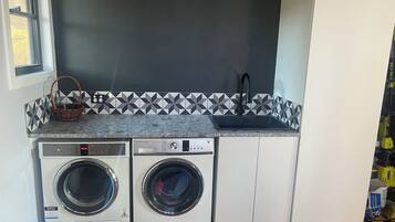 A laundry area with two front-loading washing machines, a sink, and a tiled backsplash.