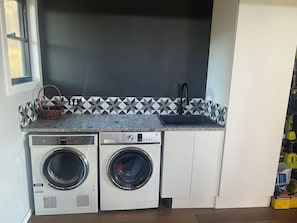 Ein Waschraum mit zwei Frontlader-Waschmaschinen, einem Waschbecken und einer gefliesten Rückwand.