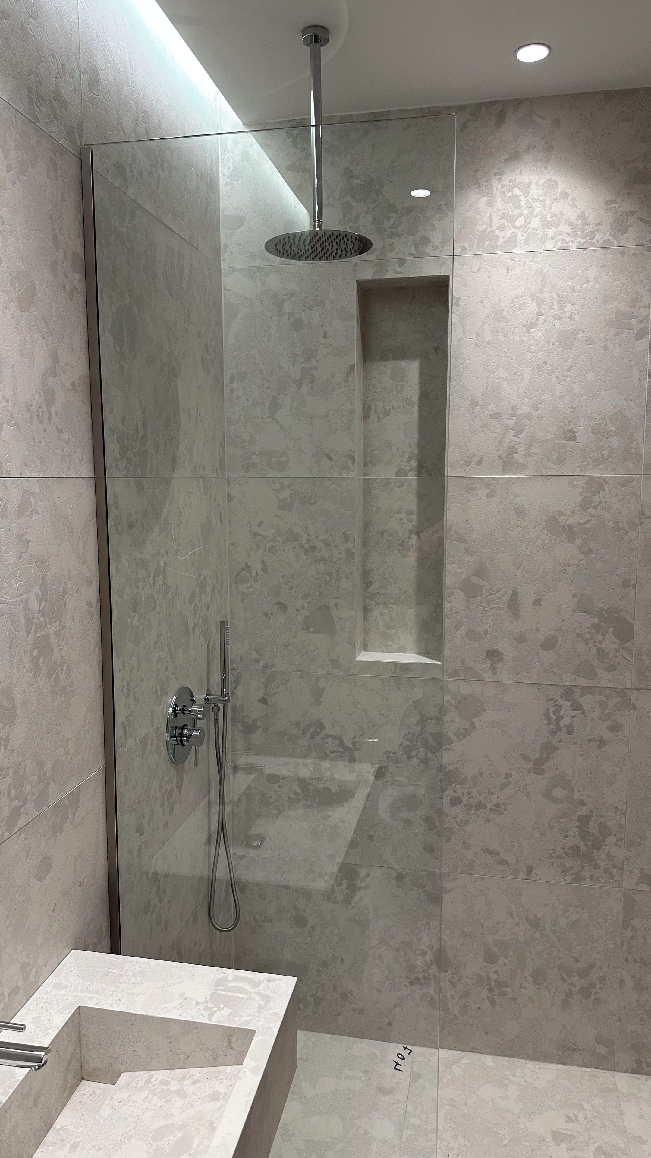 A modern bathroom with a glass-enclosed shower, a rectangular mirror, and a built-in sink.