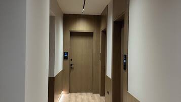 Un pasillo moderno con suelo de madera, una puerta al final y un techo con iluminación empotrada.