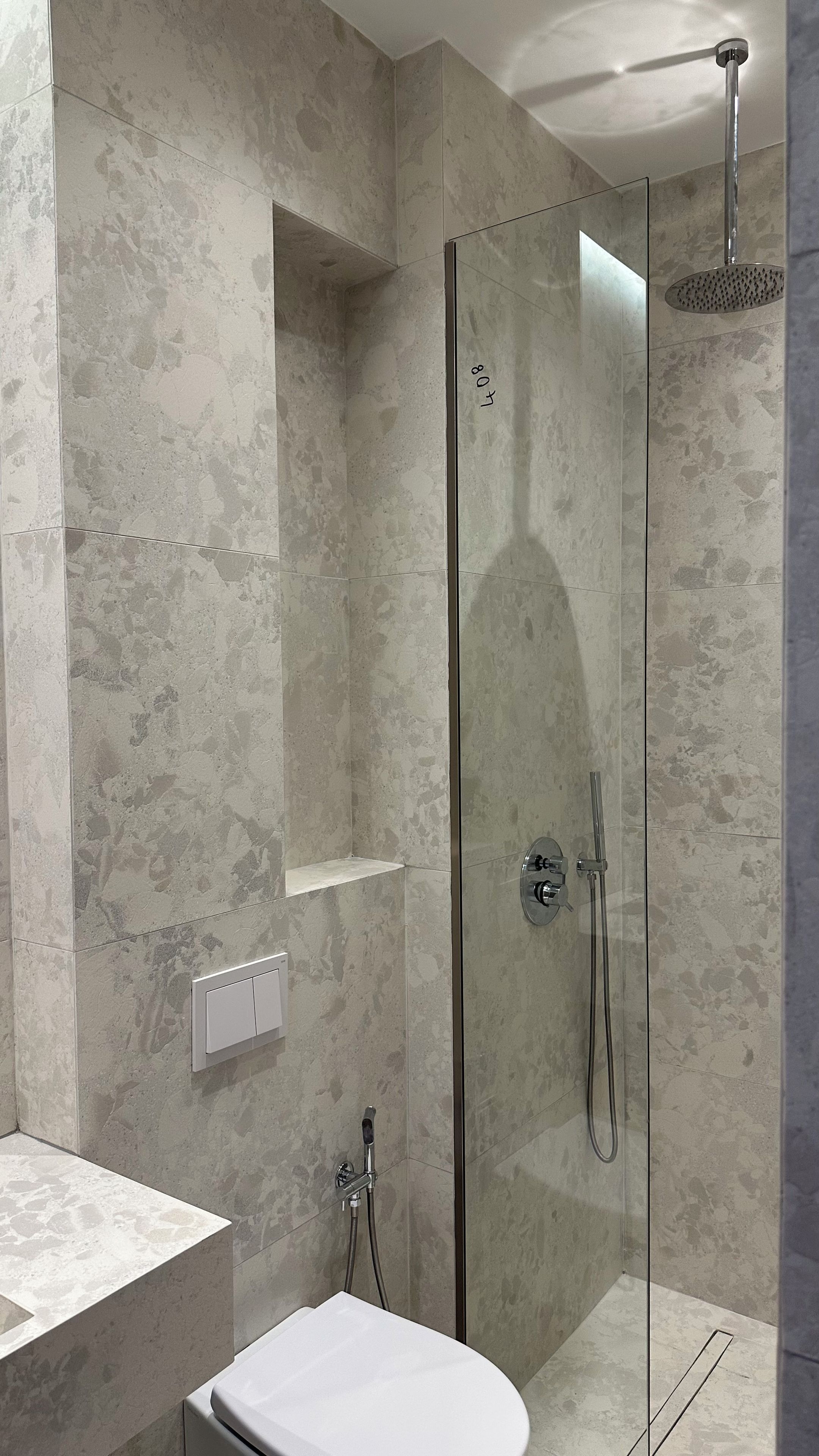 A modern bathroom with a glass-enclosed shower, a white sink, and a marble wall.
