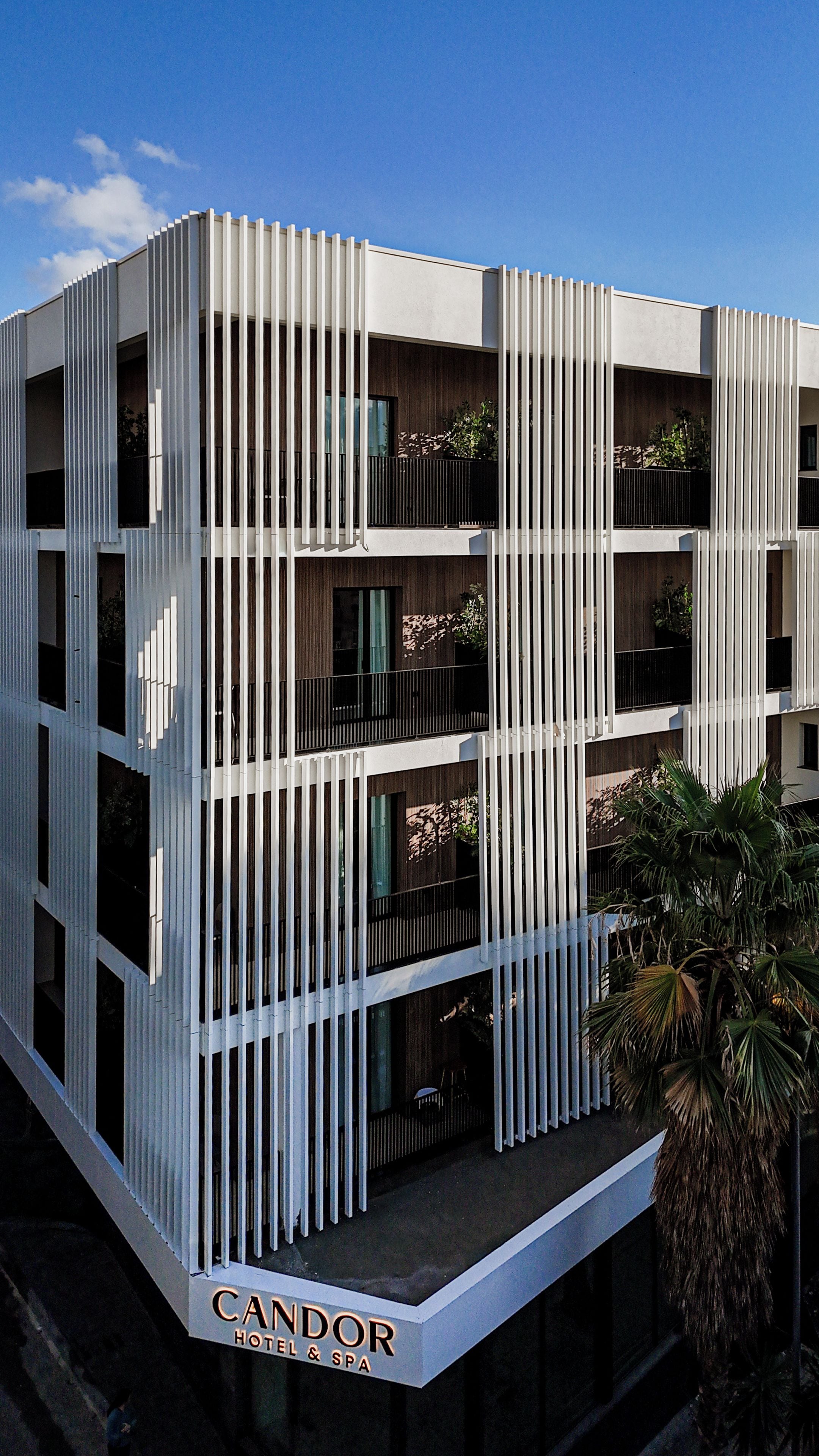 A modern hotel building with a vertical facade, balconies, and a sign indicating it is a hotel and spa.
