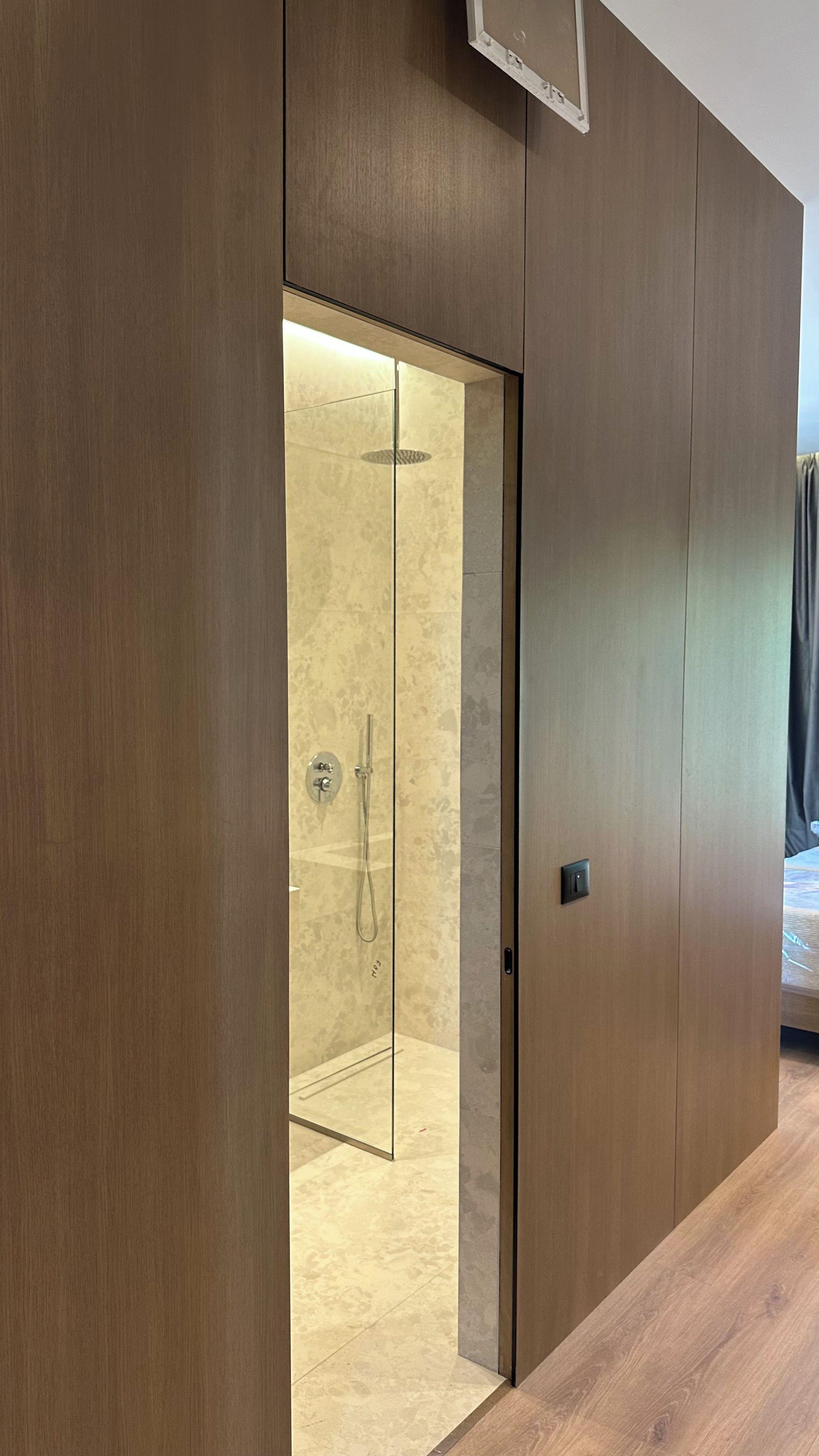 Un baño moderno con cabina de ducha de vidrio, paneles de madera y un cabezal de ducha visible.