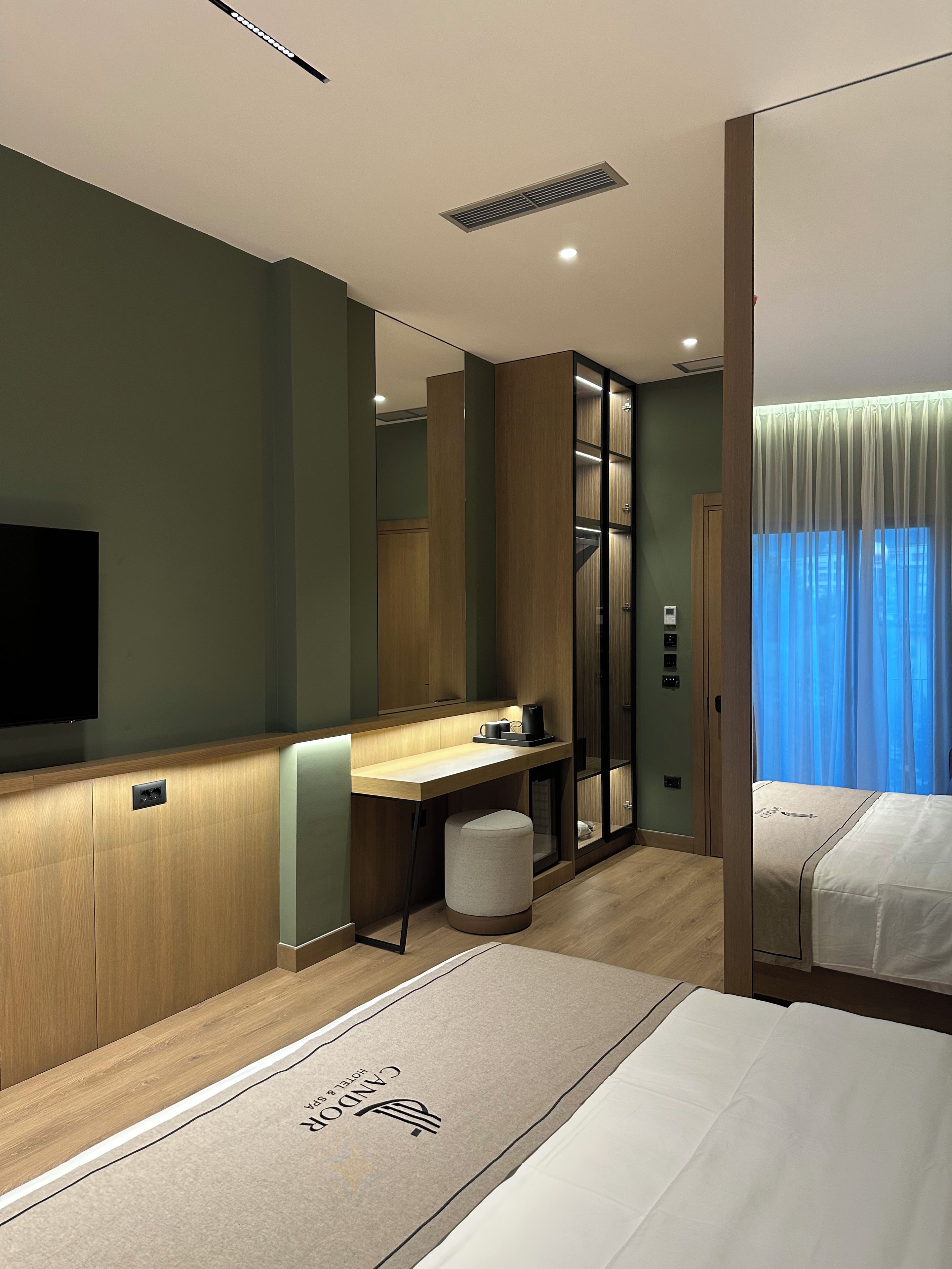 A hotel room with a bed, a desk, a mirror, a television, and a wardrobe.