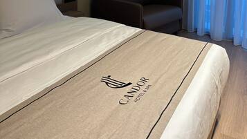 Ein Hotelzimmer mit Bett, Stuhl, Nachttisch und einem Fenster mit Vorhängen.