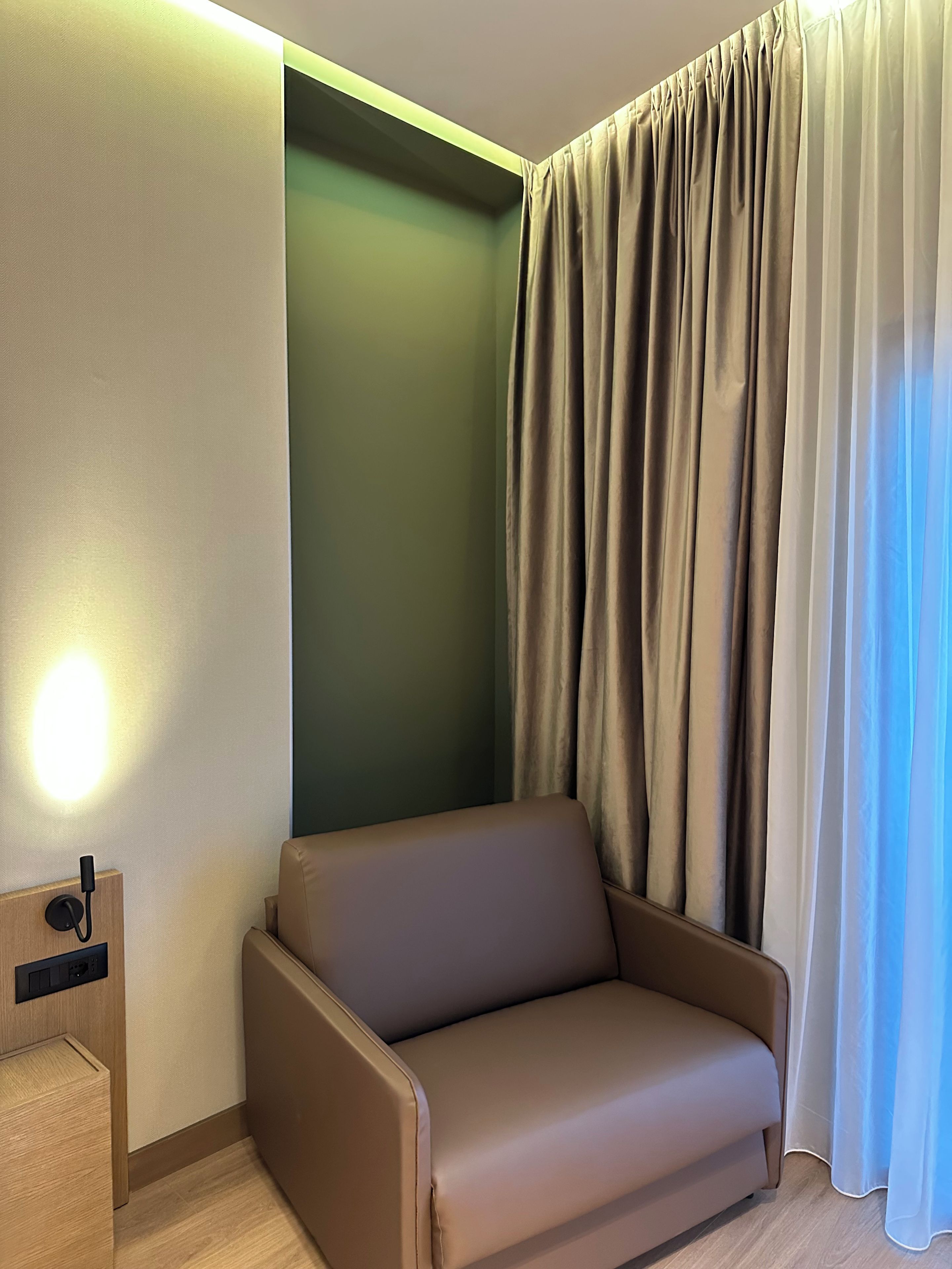 Una habitación de esquina con sofá, luz empotrada y cortina.