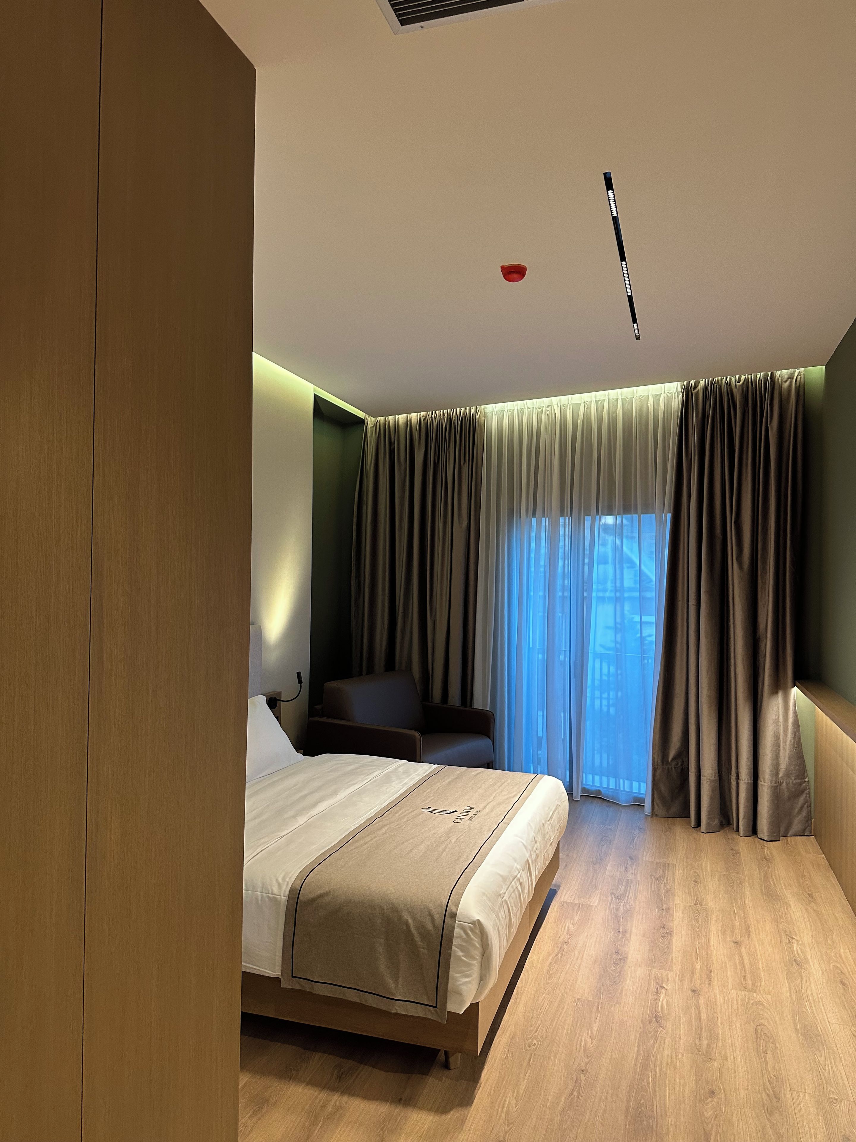 A hotel room with a bed, a chair, a desk, and a window with curtains.