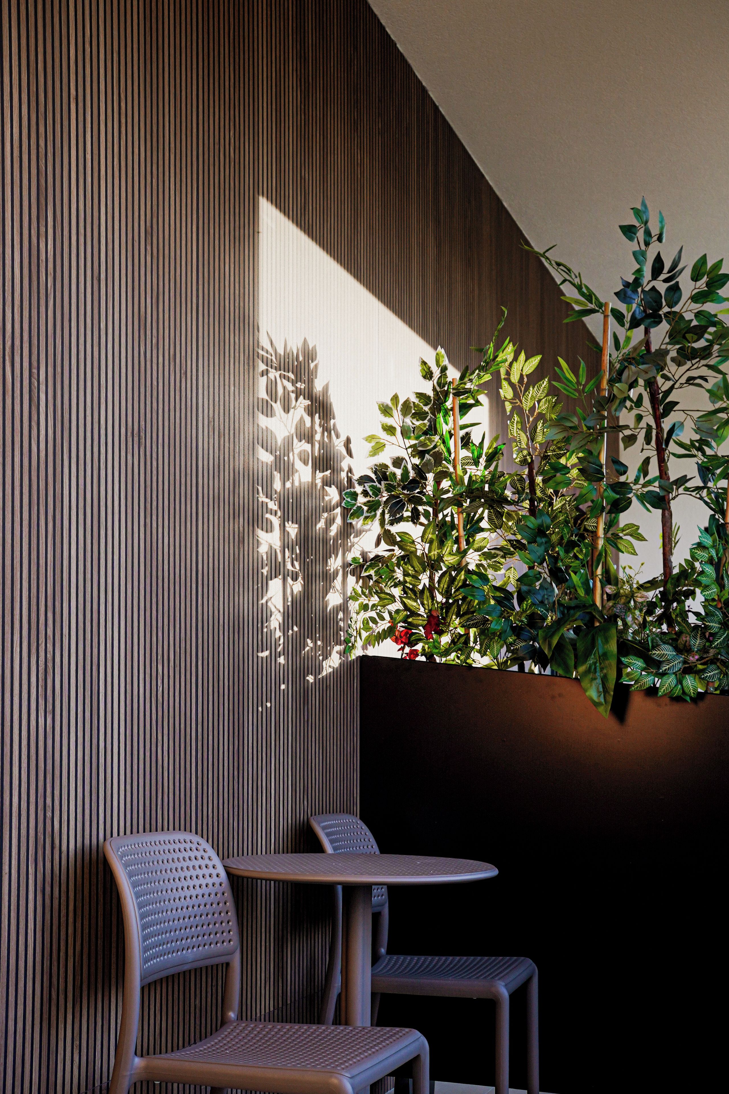 Un espacio al aire libre moderno con dos sillas, una mesa, un panel de pared de madera y una maceta con follaje verde.