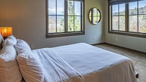 Un dormitorio con una cama grande, dos ventanas, un espejo redondo y una lámpara.