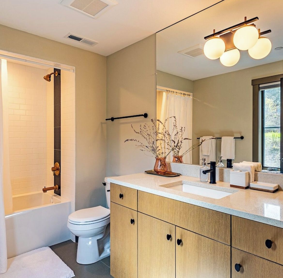A modern bathroom with a bathtub, toilet, vanity with a mirror, and a window.