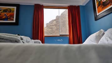 Una habitación de hotel con cama, ventana con cortinas y dos cuadros en la pared.