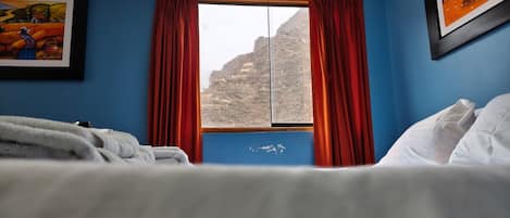 Una habitación de hotel con cama, ventana con cortinas y dos cuadros en la pared.