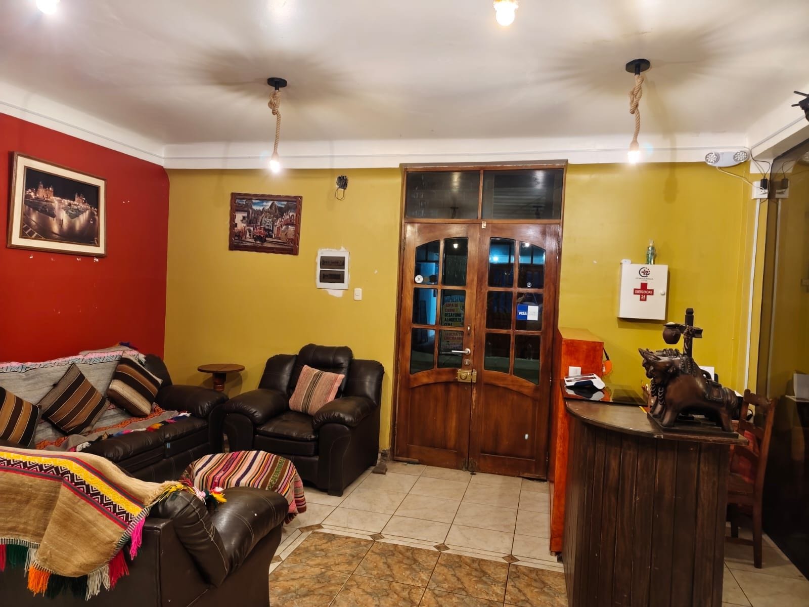 Un salón con un sofá de cuero marrón, una mesa de centro de madera y una pared roja con dos cuadros enmarcados.