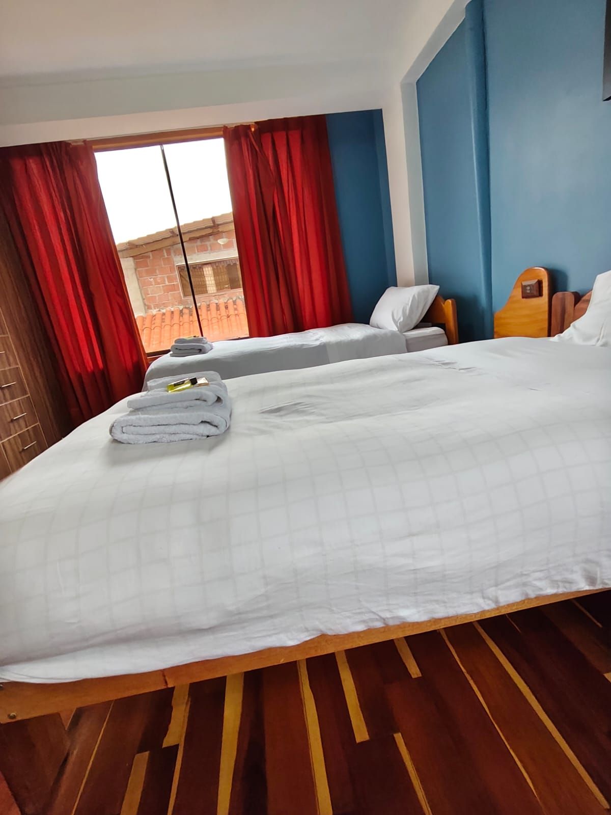 A hotel room with two beds, a wooden floor, and a view of a brick building.