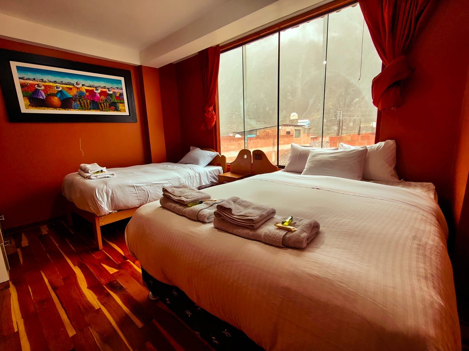 A hotel room with two beds, a large window, and a painting on the wall.