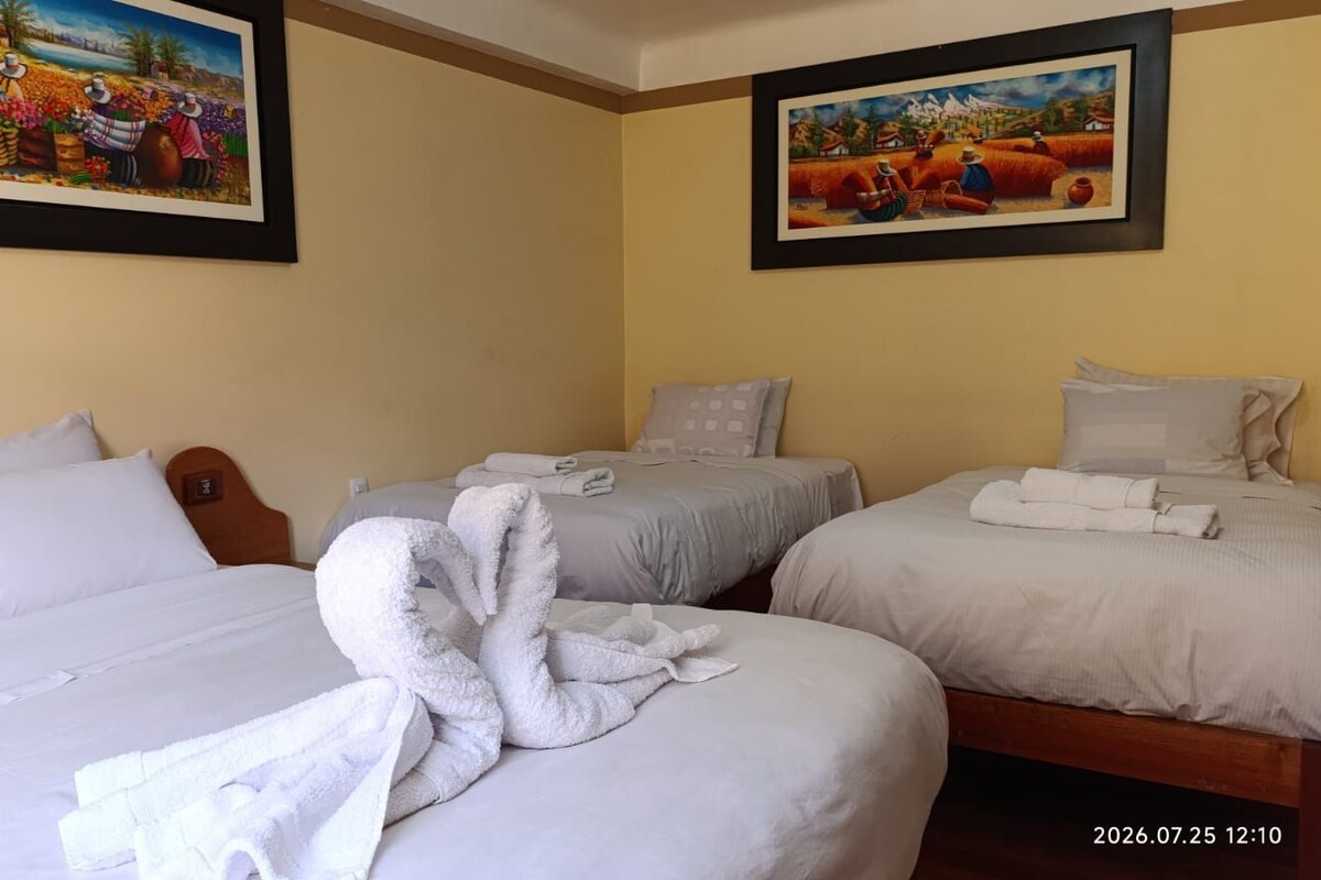 A hotel room with three beds, each with white linens and pillows. There are two paintings on the walls, one depicting a rural scene and the other a harvest.