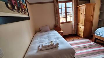 A bedroom with a single bed, a wooden wardrobe, a window with curtains, and a painting on the wall.