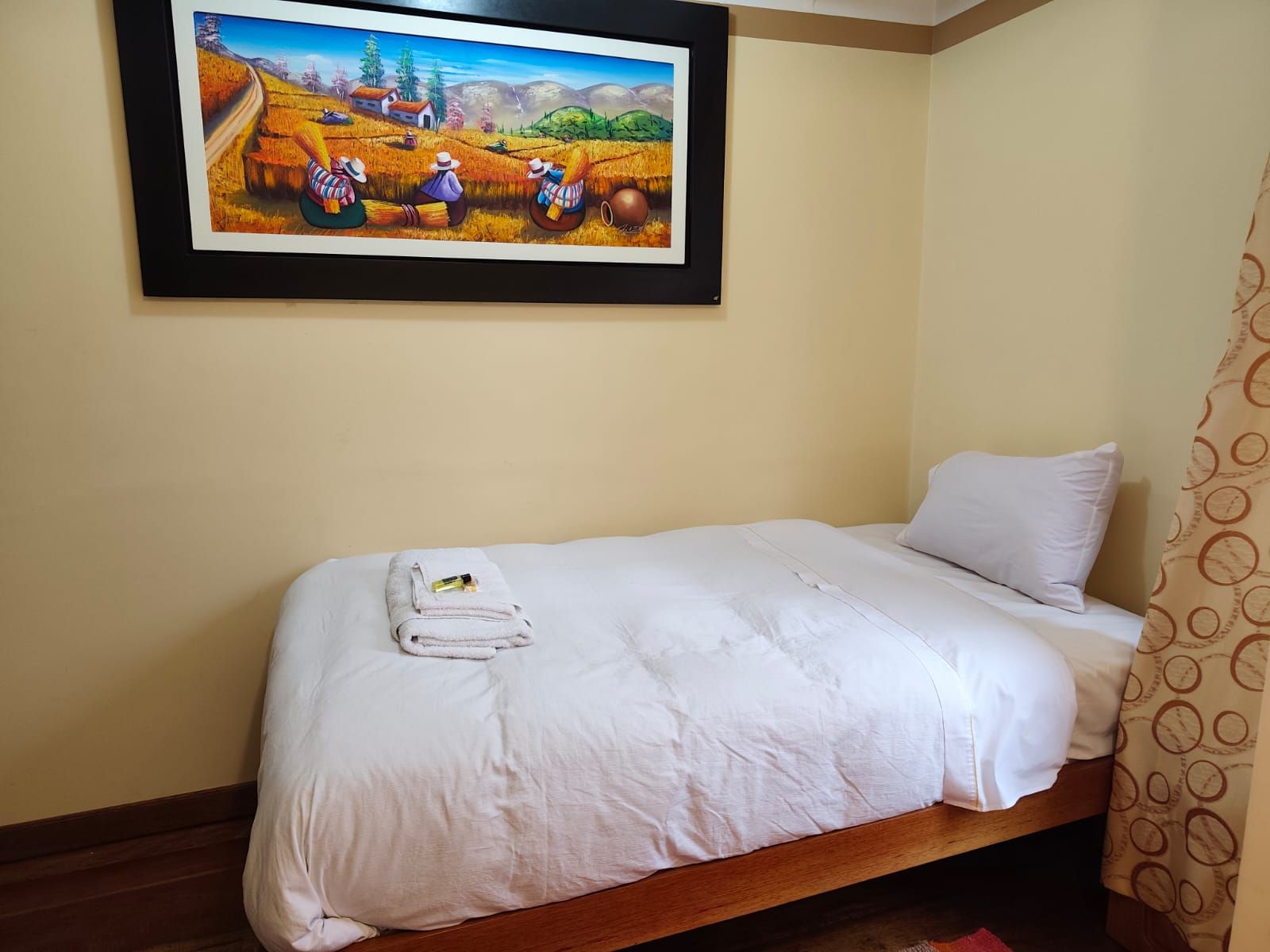 Una cama individual con edredón blanco, una toalla doblada y una pequeña botella encima.
