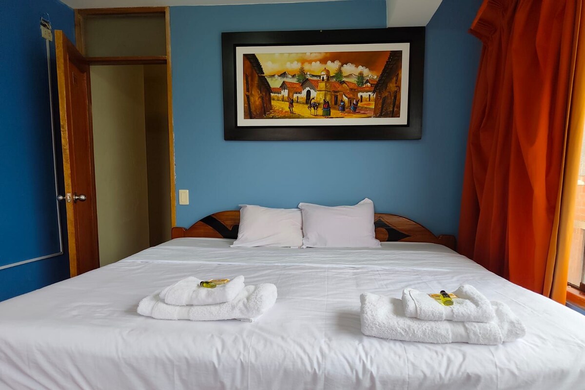 A hotel room with a bed, white linens, a painting on the wall, and a door.