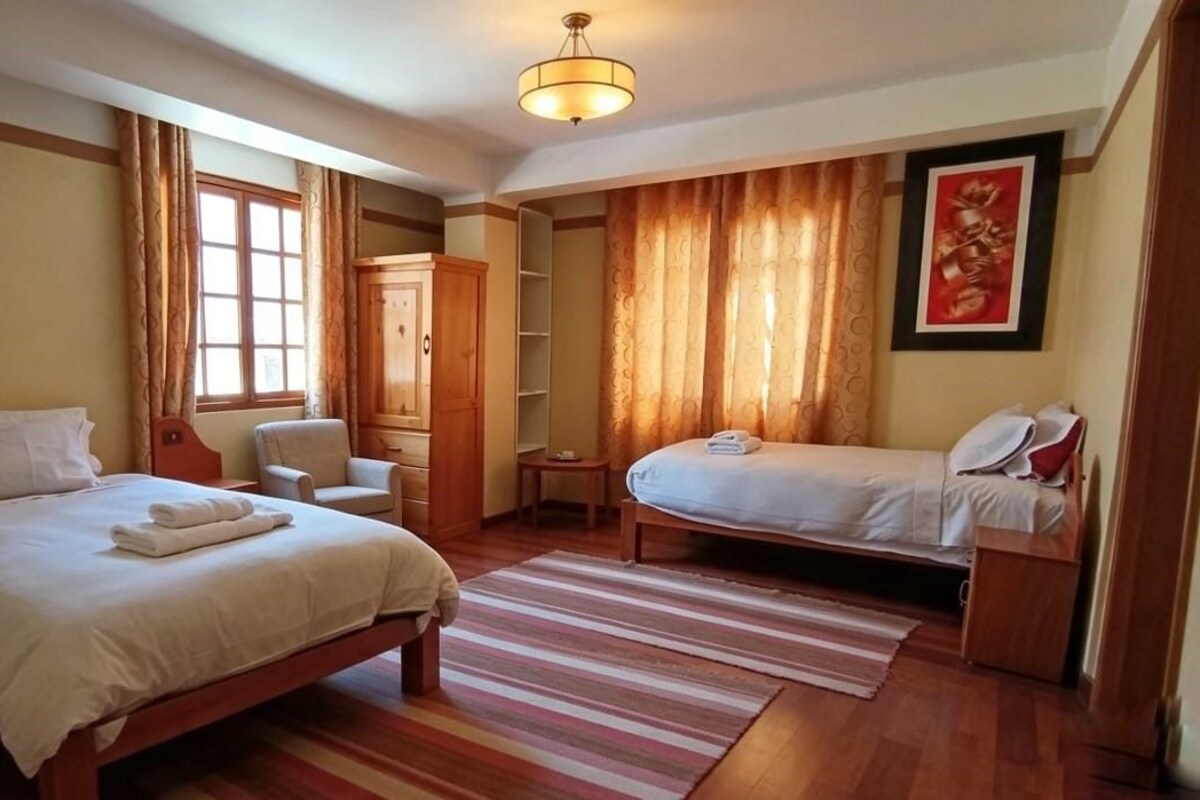 A hotel room with a large bed, a smaller bed, a chair, a wardrobe, and a desk.