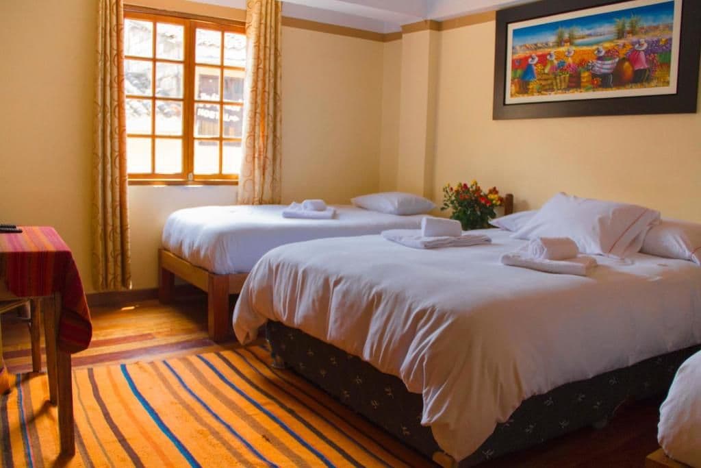 Habitación de hotel con dos camas, una ventana con cortinas, un cuadro en la pared y una alfombra a rayas.