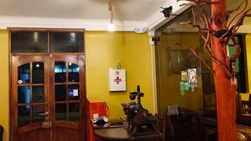 Quarto com porta de madeira, mesa redonda com um objeto decorativo, ventoinha no teto e luminária fixada na parede.