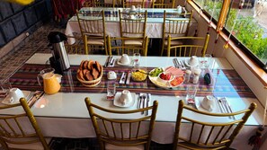 Une table à manger dressée avec des assiettes, des couverts et une carafe de jus d’orange.