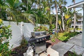 En kolgrill i ett vackert utomhusområde med palmer och ett vitt staket.
