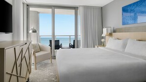 Ein Hotelzimmer mit einem großen Bett, einem Schreibtisch, einem Sessel, einem Fernseher und Blick auf den Ozean.