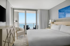 Une chambre d’hôtel avec un grand lit, un bureau, une chaise, une télévision et une vue sur l’océan.