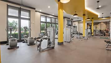 A gym with various exercise machines, large windows, and a yellow accent wall.