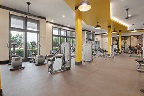 A gym with various exercise machines, large windows, and a yellow accent wall. - King Suite | Walk to Toyota Stadium | Pool + Gym (Frisco)