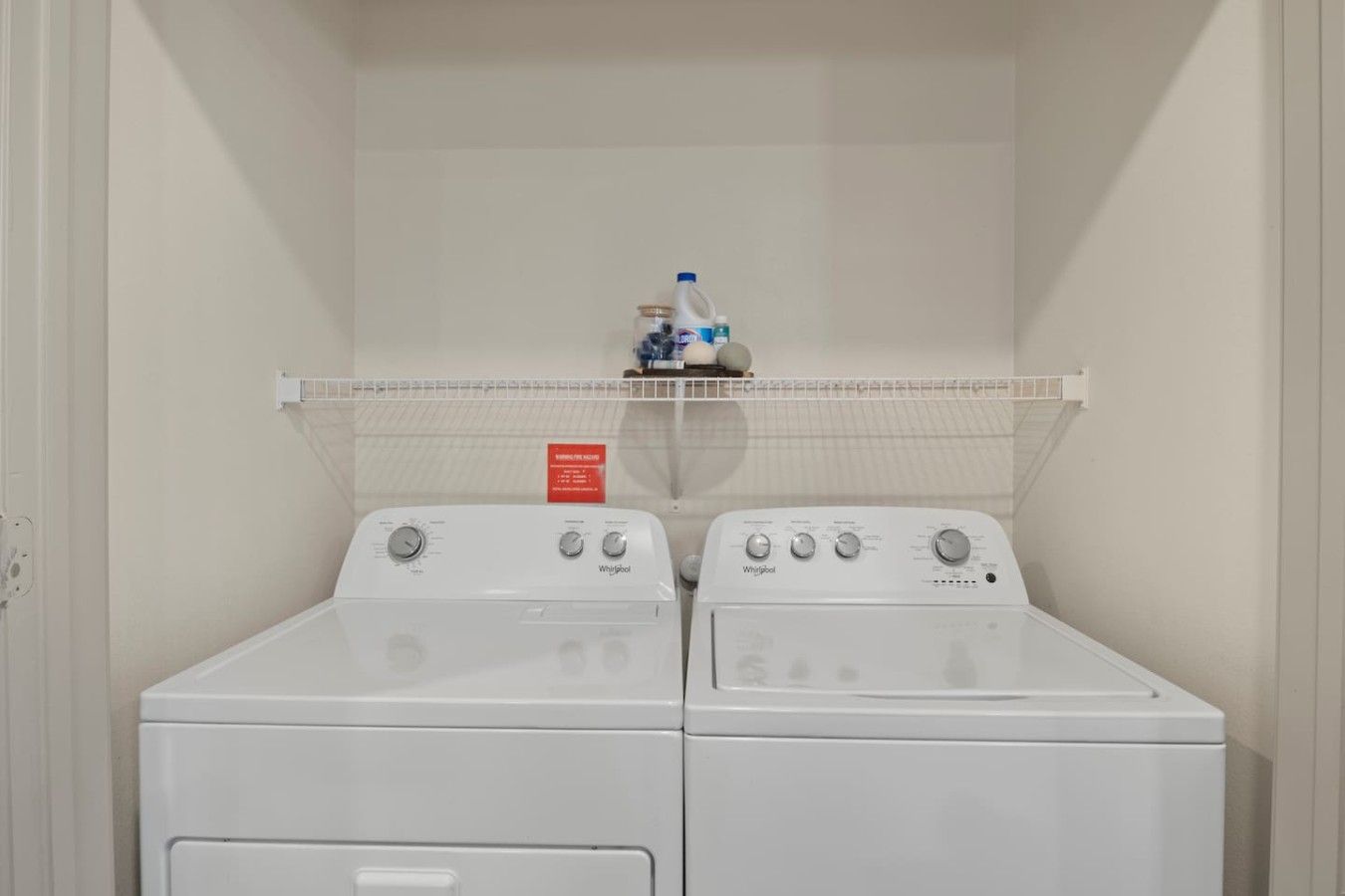 Lavanderia dotata di due lavatrici a carica frontale Whirlpool e uno scaffale sovrastante con prodotti per la pulizia.