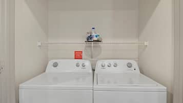 Lavanderia dotata di due lavatrici a carica frontale Whirlpool e uno scaffale sovrastante con prodotti per la pulizia.