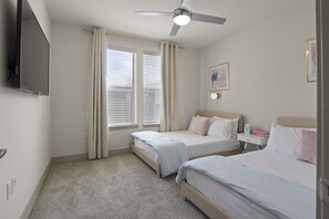 A hotel room with two beds, a ceiling fan, a flat-screen TV, and a bedside table with a lamp.