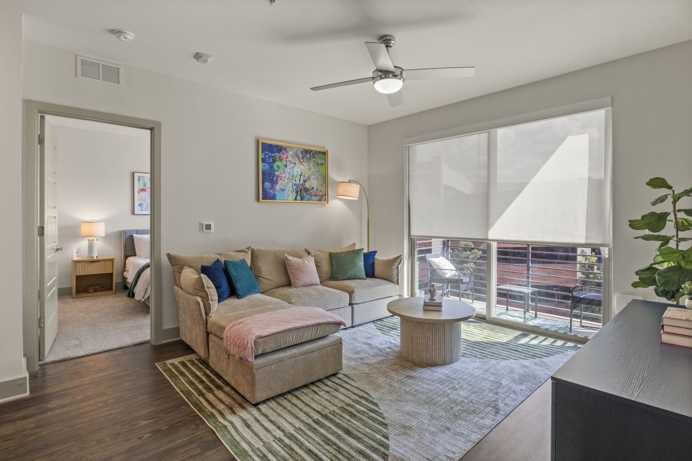 A modern living room with a sofa, a coffee table, a ceiling fan, and a large window overlooking a balcony.