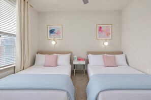 A hotel room with two beds, each with a headboard, a bedside table with a lamp, and two framed abstract paintings on the wall.