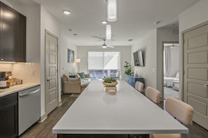 Una cocina moderna con una isla grande, un comedor con mesa y un salón con sofá y vistas al balcón.