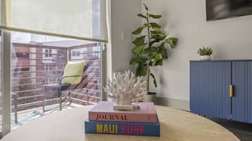 Ein Zimmer mit großem Fenster, einer Pflanze, einem Bücherregal voller Bücher und einem blauen Schrank.