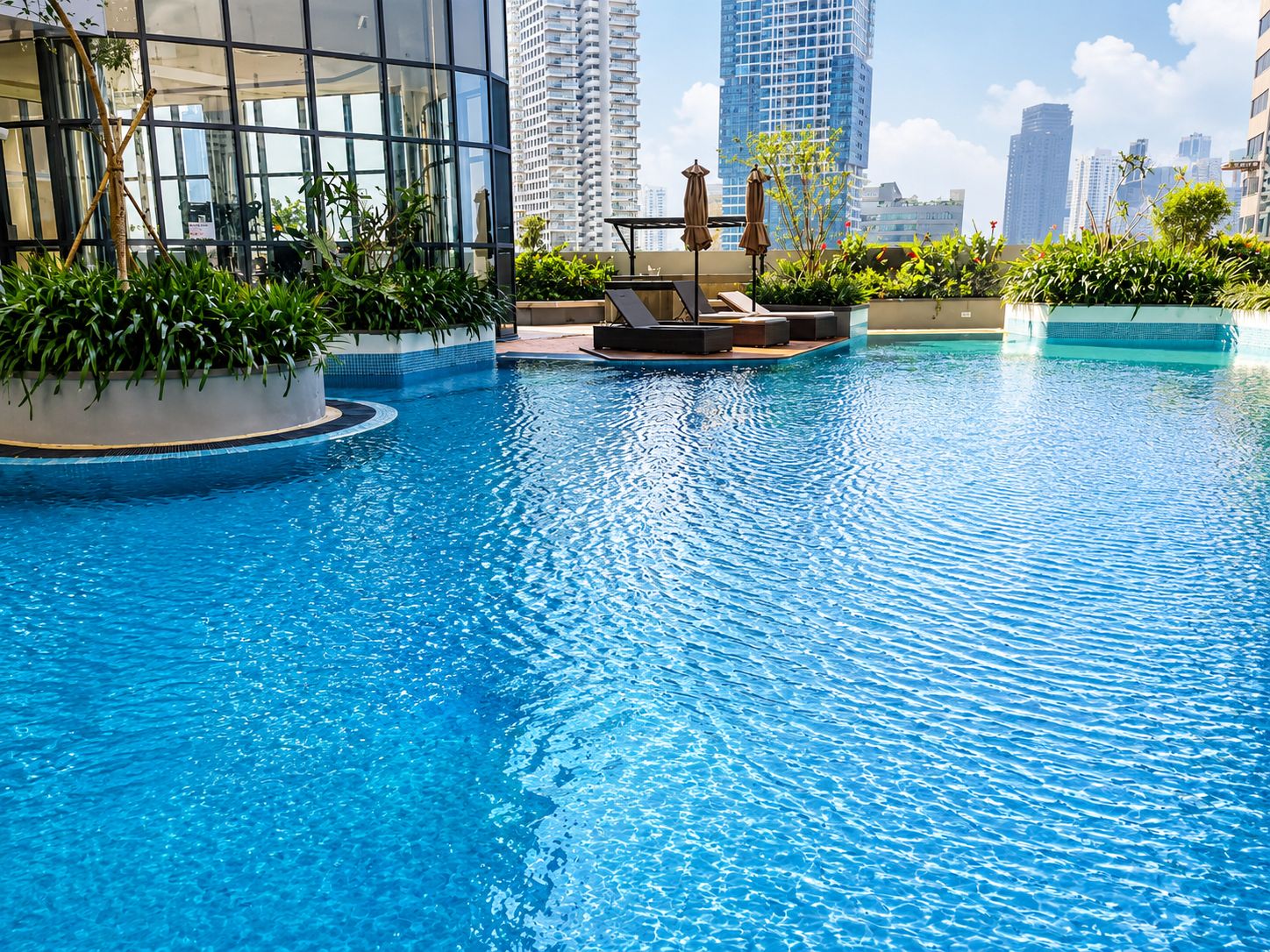 Piscina con sillas de descanso y jardineras, rodeada de edificios altos.