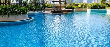 Piscina con sillas de descanso y jardineras, rodeada de edificios altos.