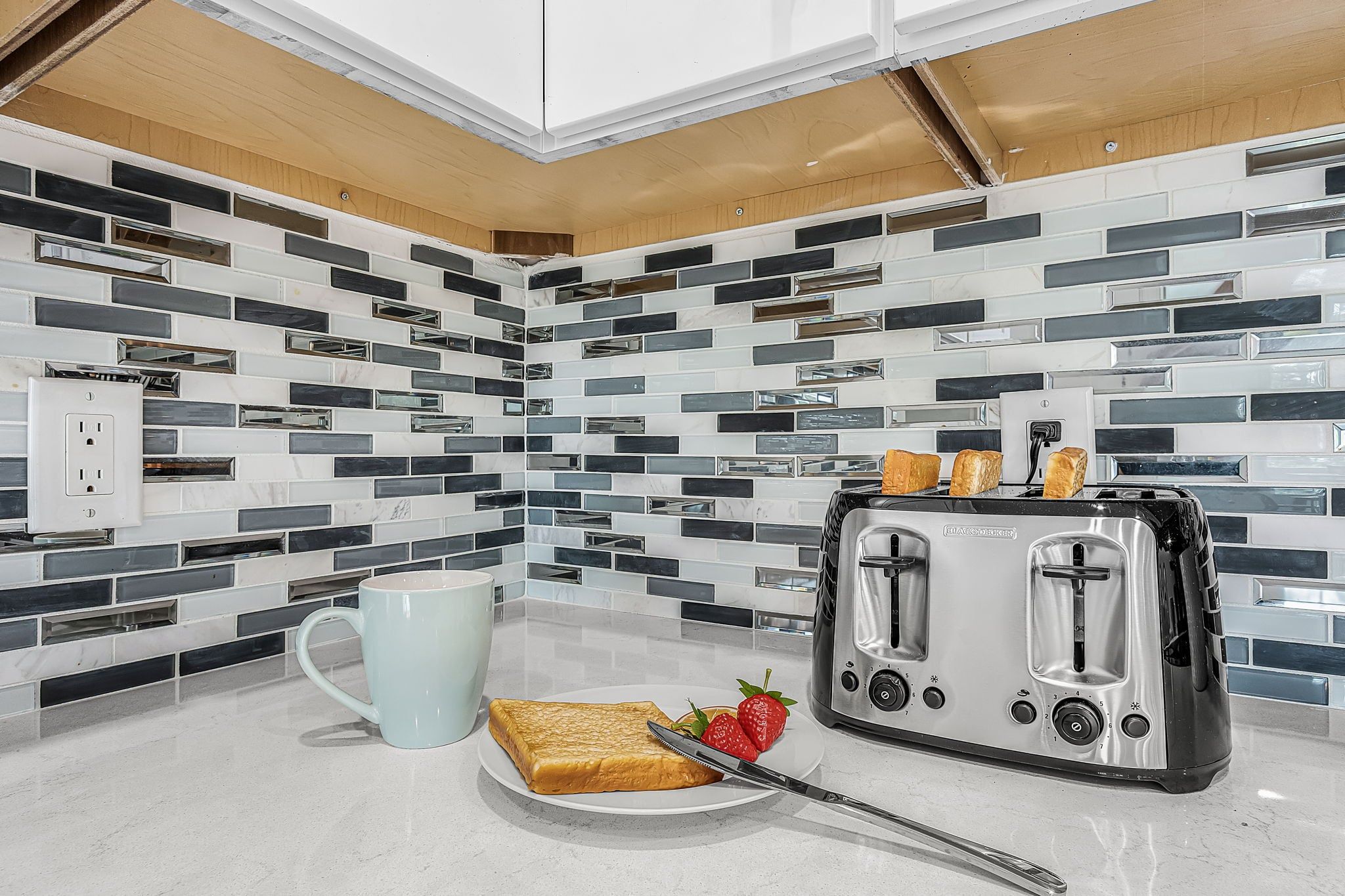 A kitchen with a modern design, featuring a toaster, a mug, and a plate with toast and strawberries.