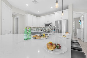 Una cocina moderna con armarios blancos, electrodomésticos de acero inoxidable y una isla central con alimentos.