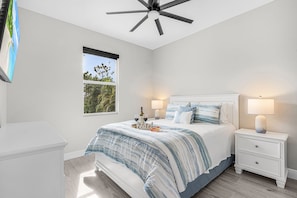 A bedroom with a bed, bedside tables, a ceiling fan, a window, and a view of greenery outside. - Sunrise Oasis Pool Escape with Views and Fun for the Whole Family - Villa Sunrise Oasis - Roelens (Cape Coral)