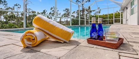 Un espace aménagé au bord de la piscine, avec une serviette, deux bouteilles et un verre d’eau.