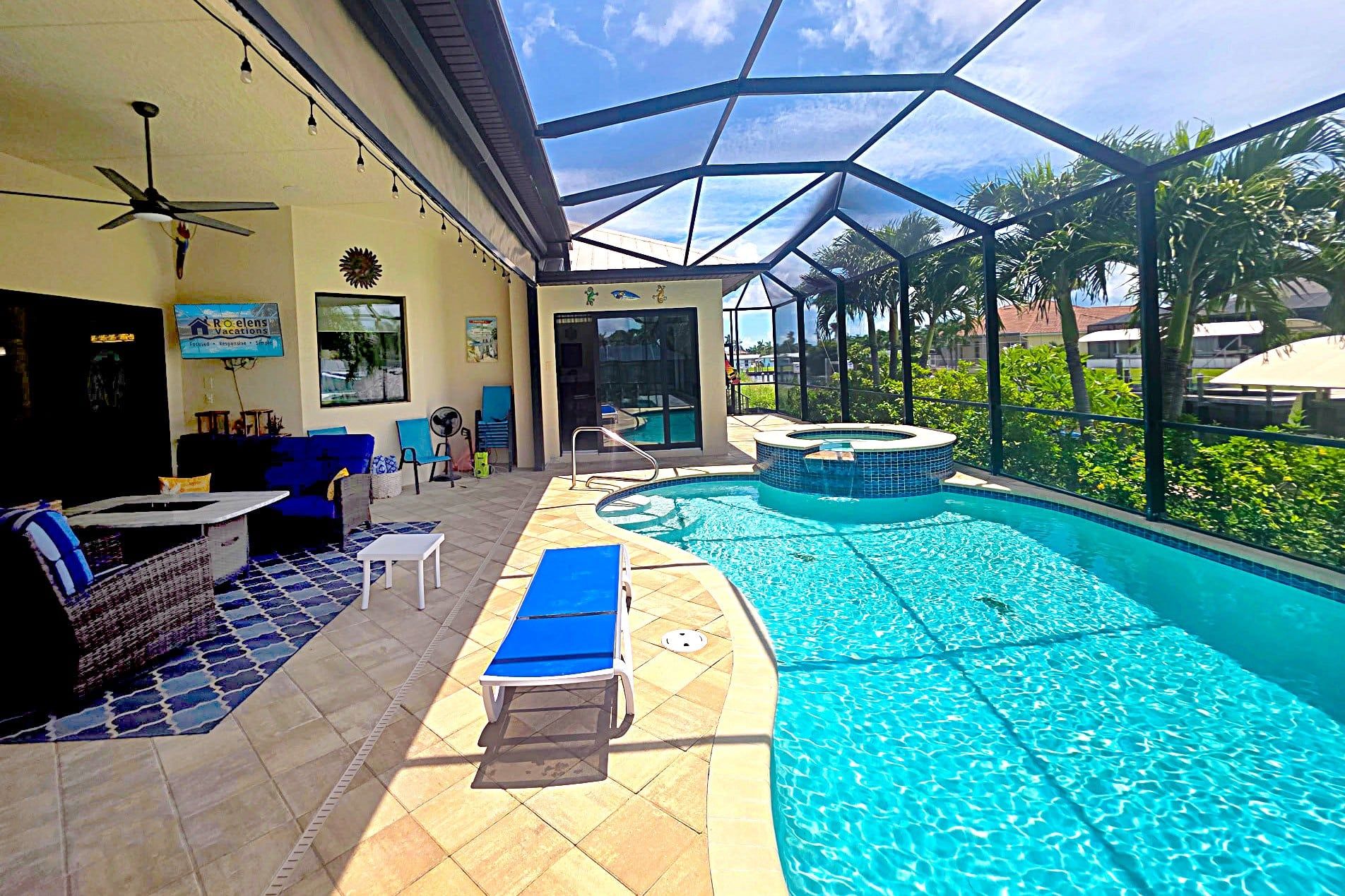 An indoor swimming pool with a glass ceiling, lounge chairs, and a ceiling fan.