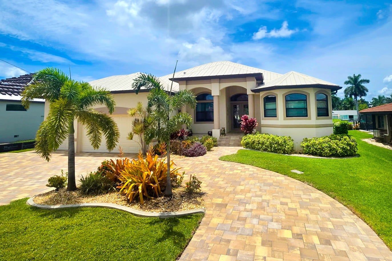 A two-story house with a paved driveway, palm trees, and well-maintained landscaping.